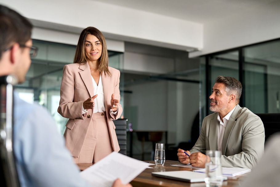 Business meeting with presenter pointing at charts on a screen in a bright conference room