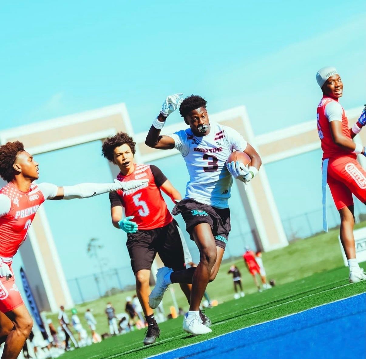 Football players running on a field, with one in a white jersey catching a pass near the end zone.