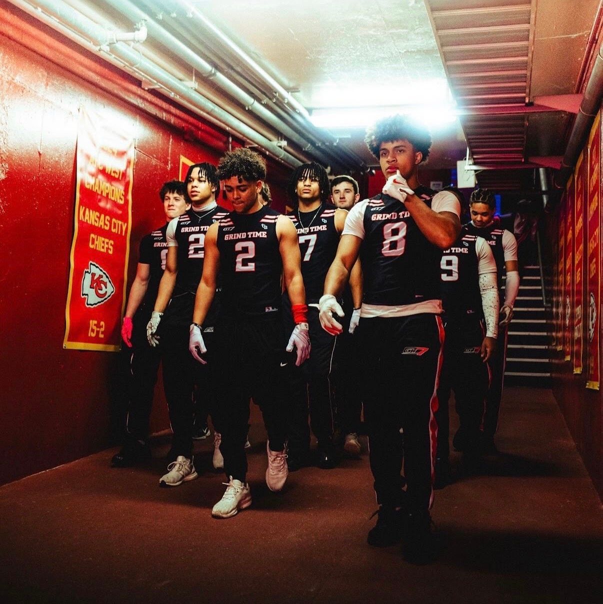 Football players in black uniforms walking through a red-lit tunnel toward the field
