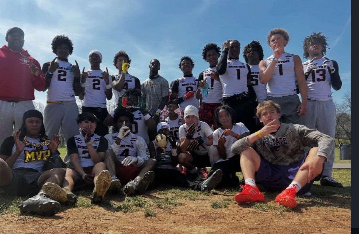 Youth football team posing on a grassy field under a clear blue sky, wearing white jerseys and black shorts.