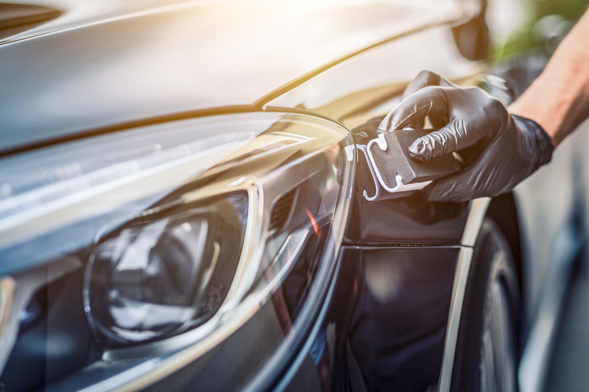 Person polishing a white car hood with a black and yellow electric polisher.