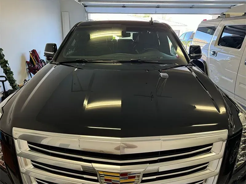 Black Cadillac SUV in a garage, reflecting overhead lights.