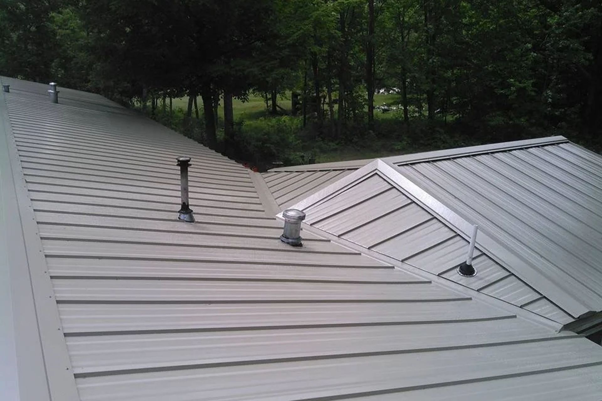 A metal roof with a chimney on it and trees in the background