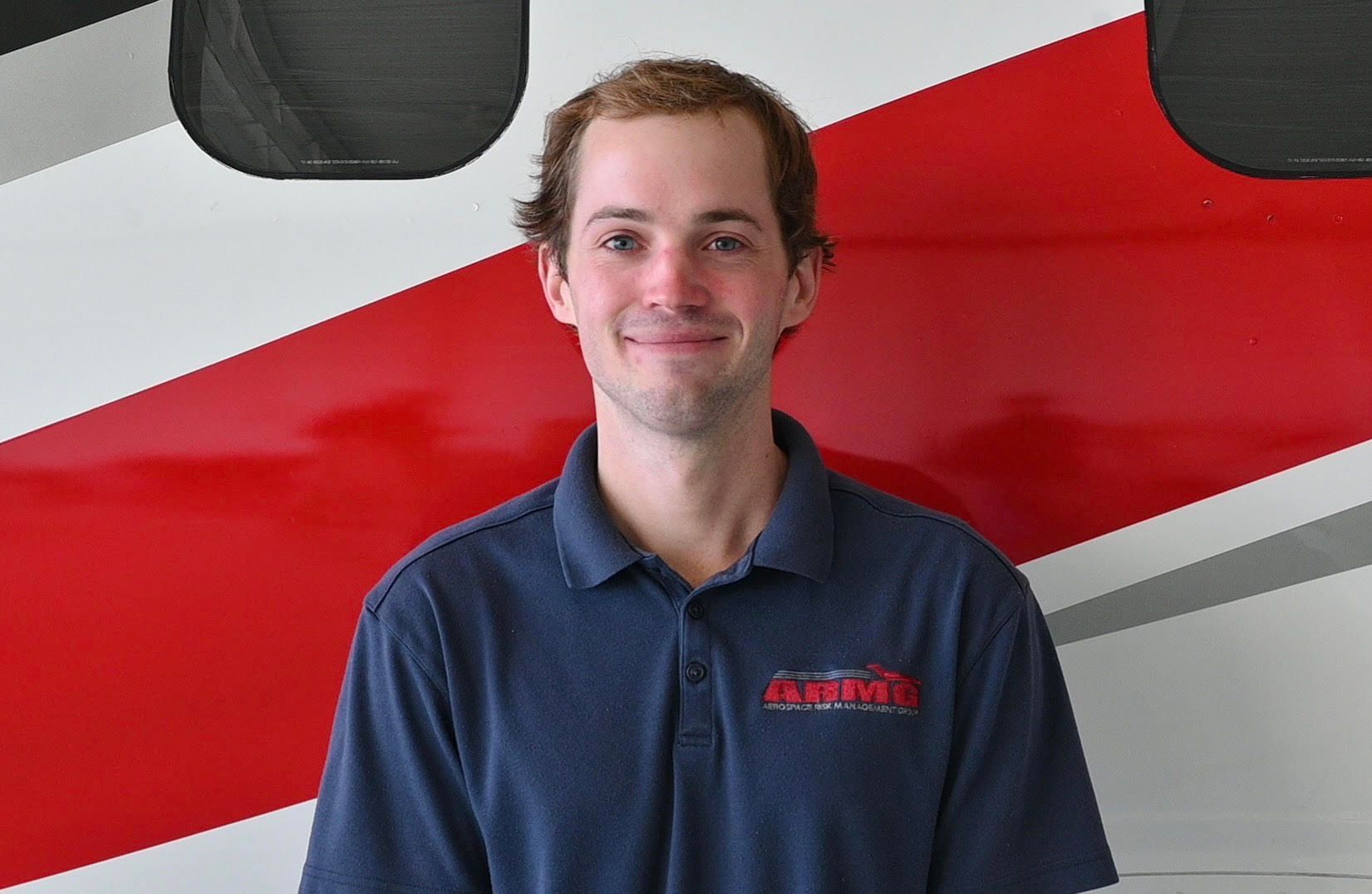 A man in a blue shirt is smiling in front of a red and white striped wall.