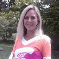 A woman in an orange and purple shirt is standing in a park.