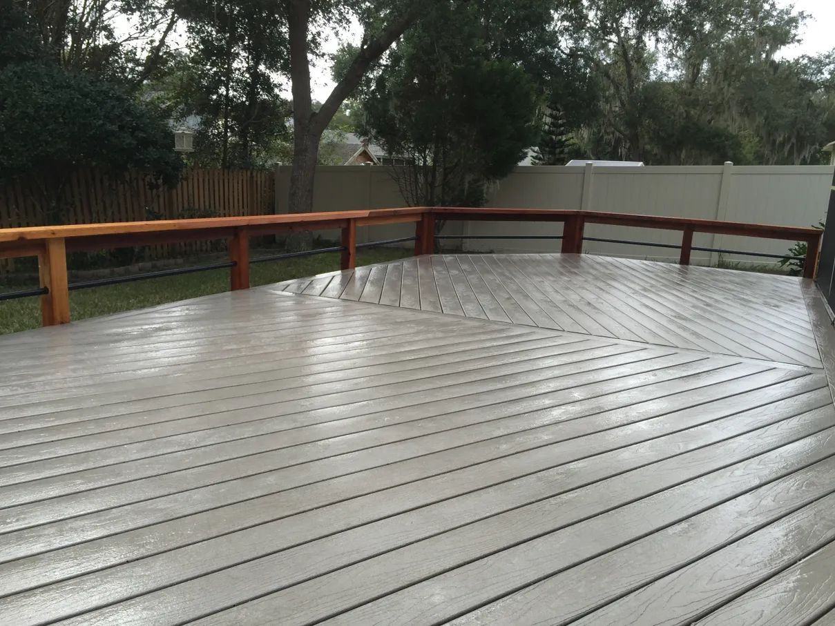A wooden deck with a wooden railing and a fence in the background