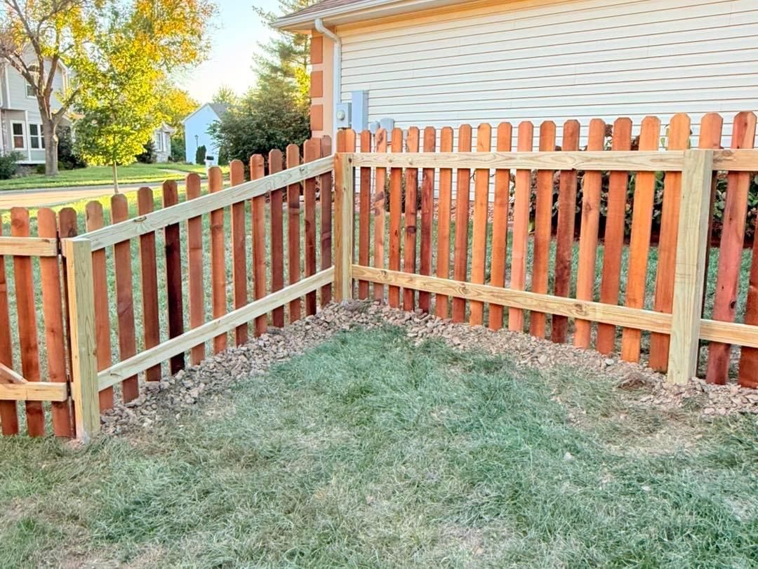 A wooden picket fence is in the backyard of a house.