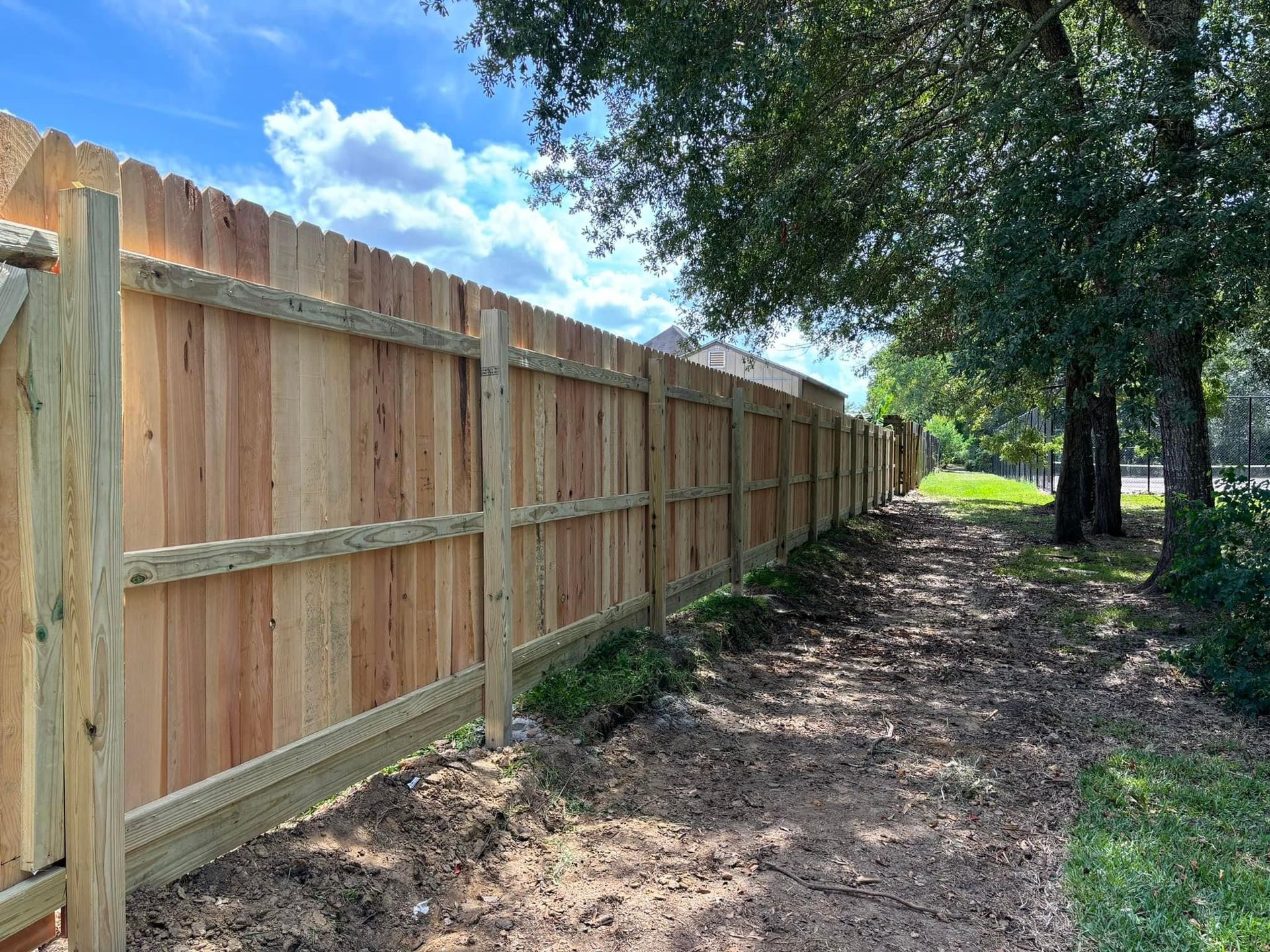 A wooden fence along a dirt path with trees in the background.