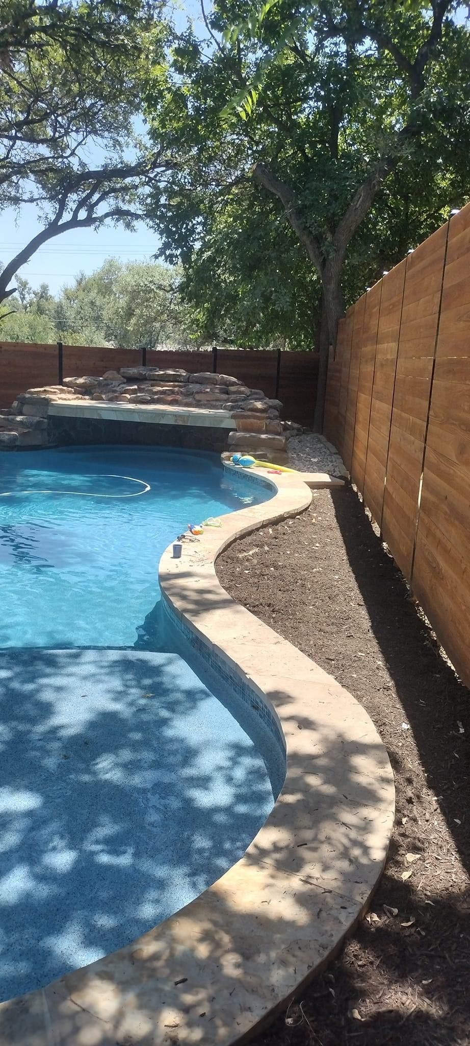A wooden fence surrounds a large swimming pool.