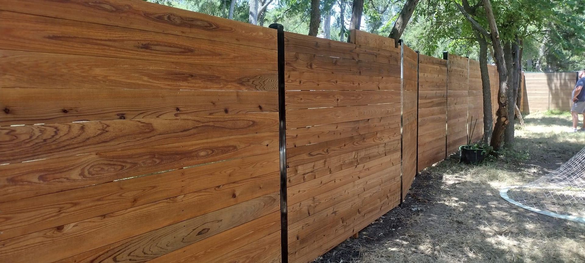 A wooden fence is surrounded by trees in a yard.