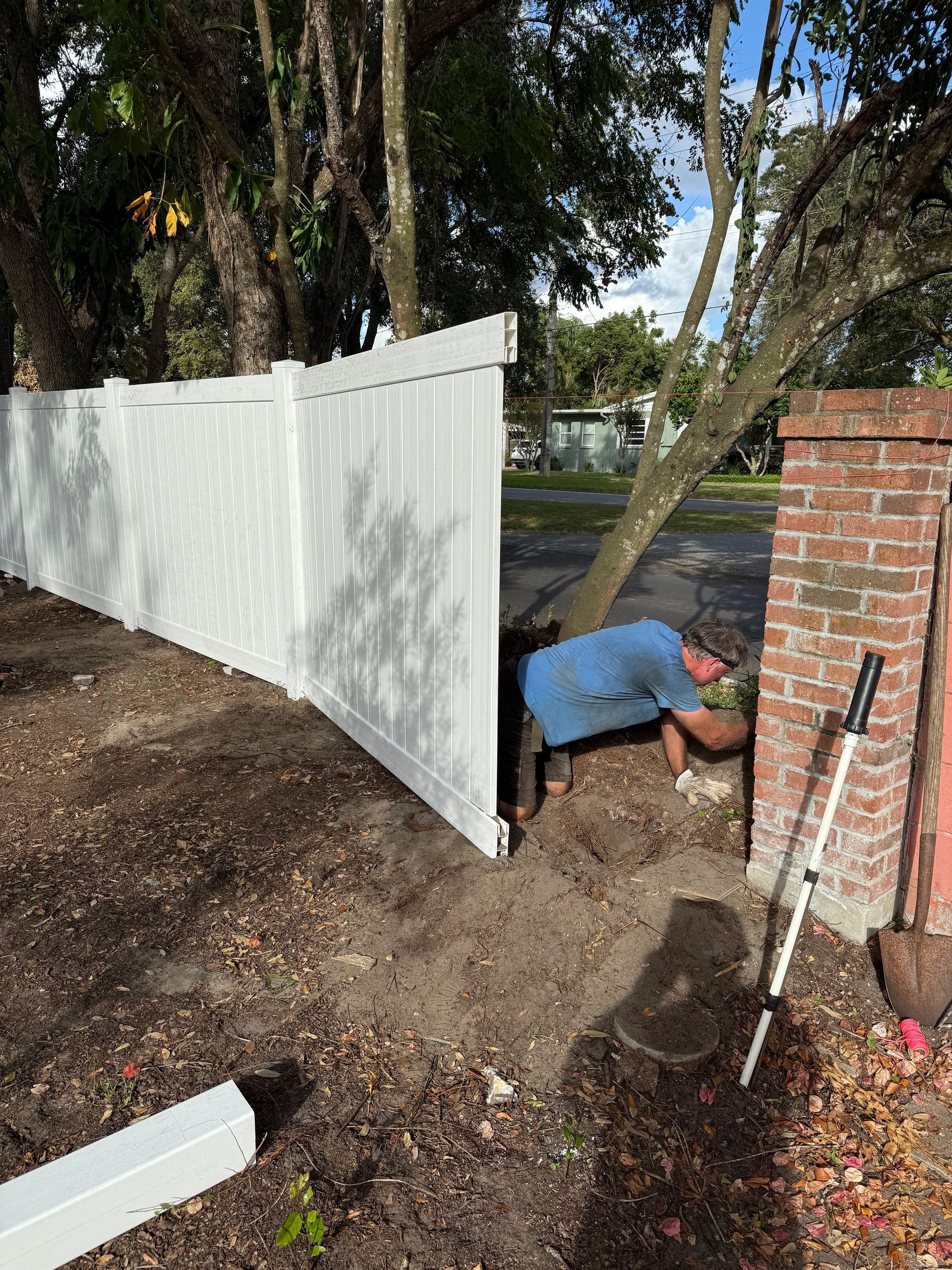 A man is digging in the dirt next to a white fence.