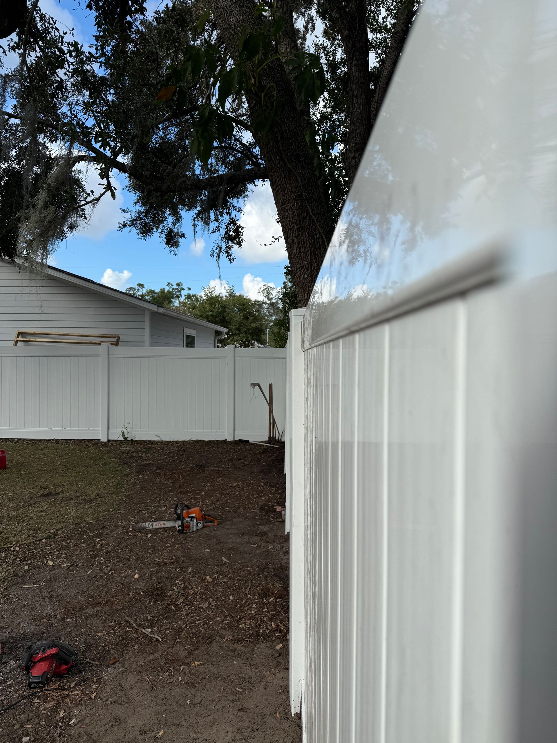 A white fence with a tree in the background and a house in the background.
