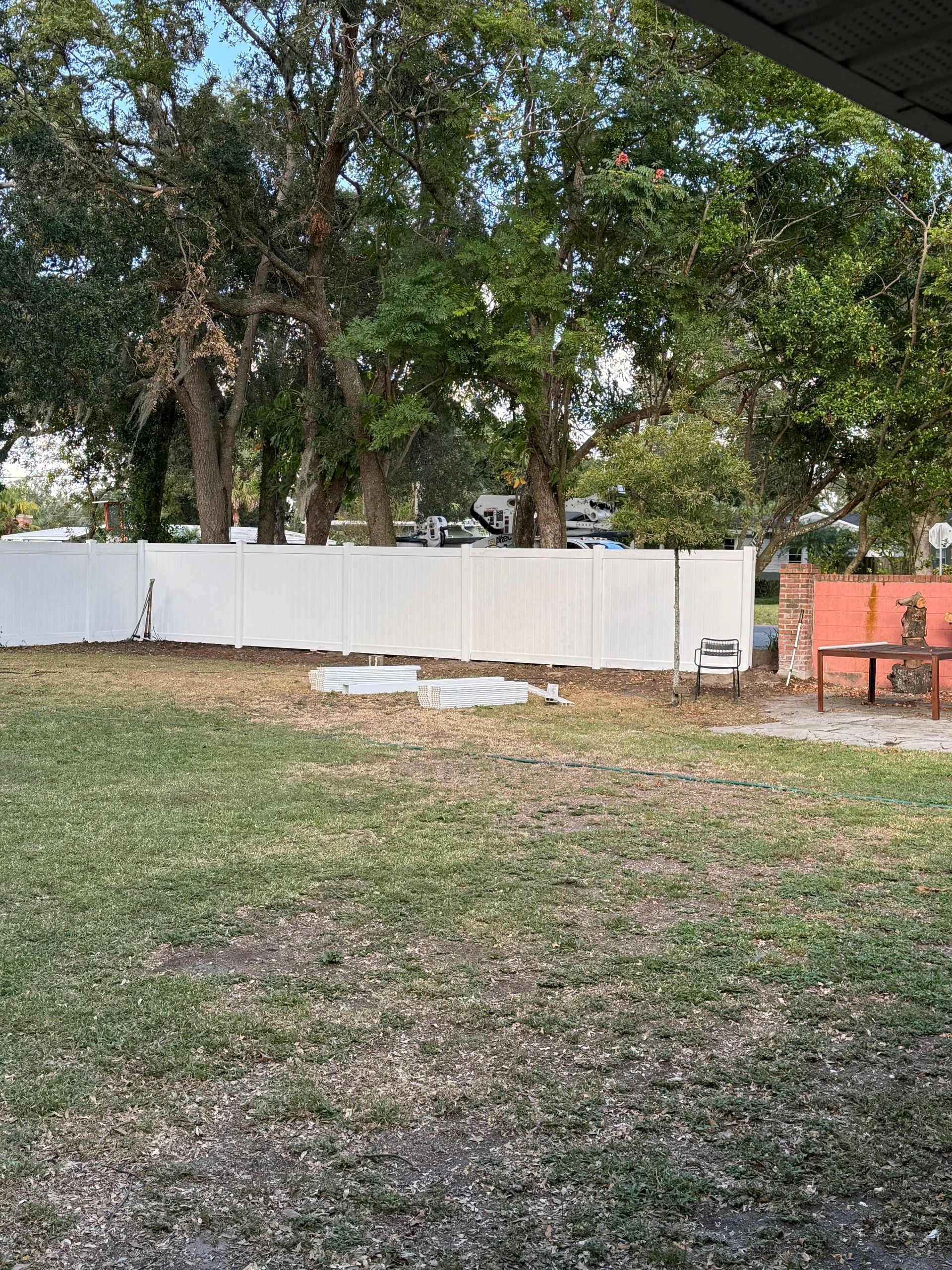 A backyard with a white fence and trees in the background.