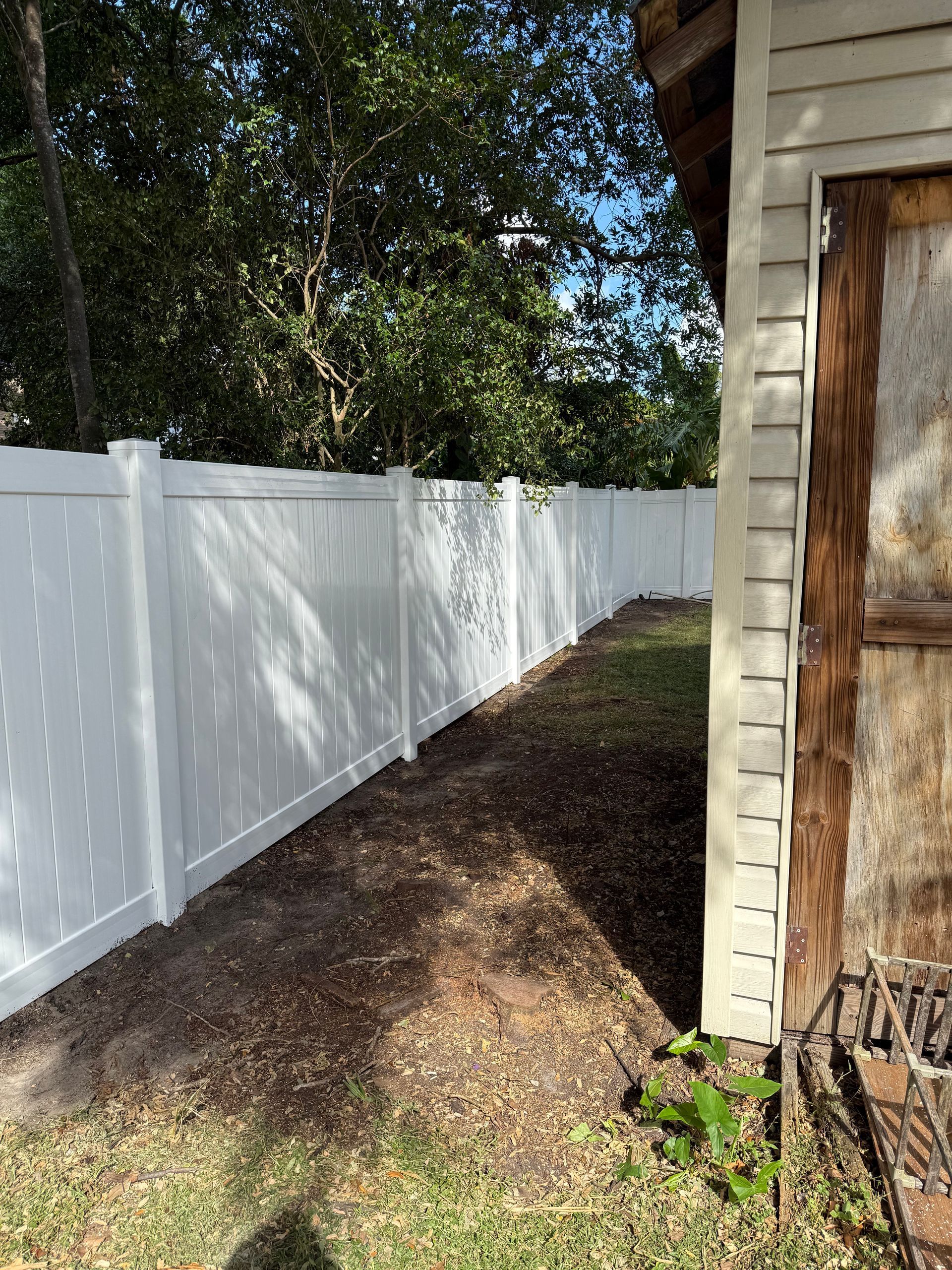 A white fence is surrounding a shed in a backyard.