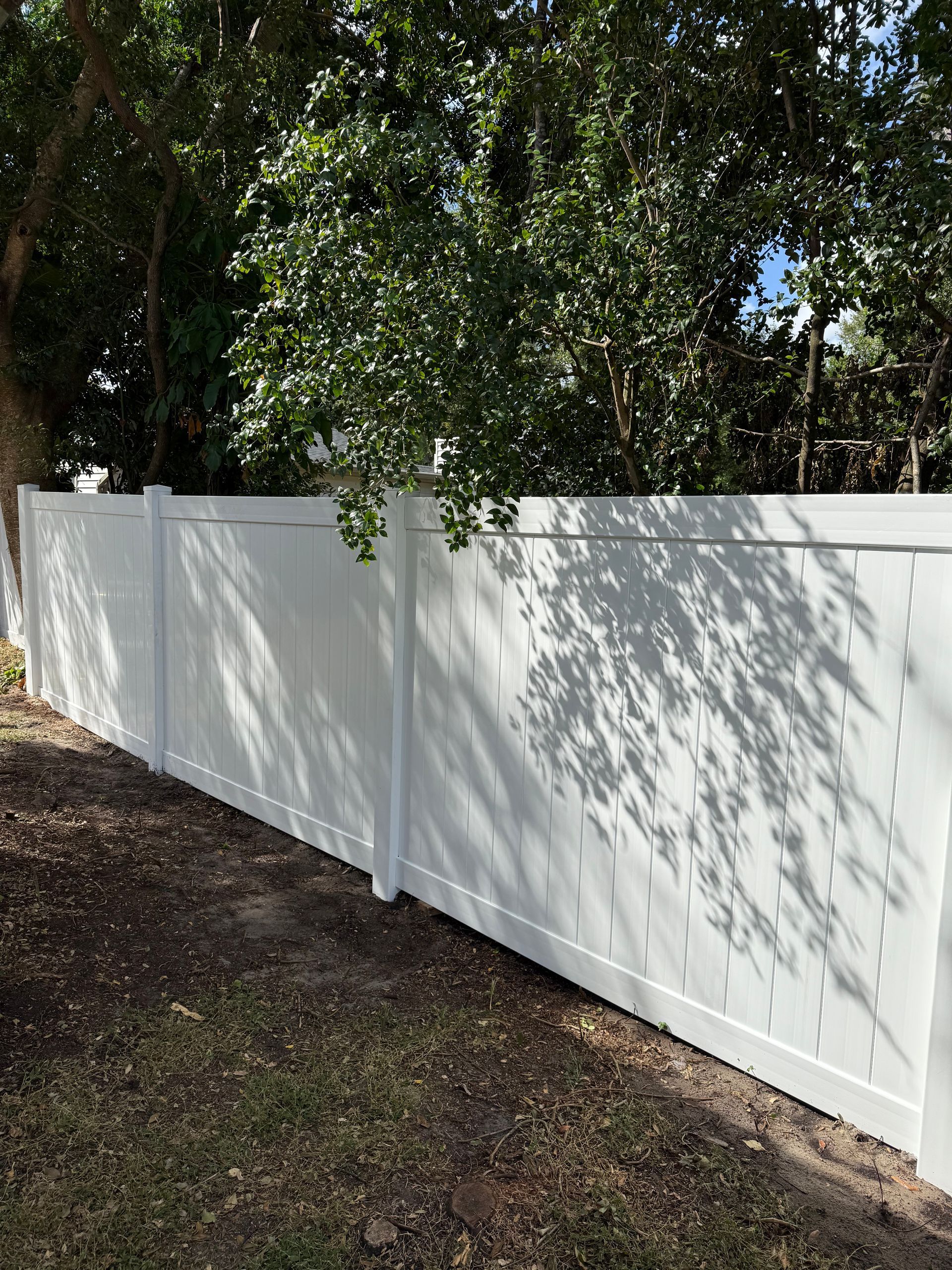 A man is digging in the dirt next to a white fence.