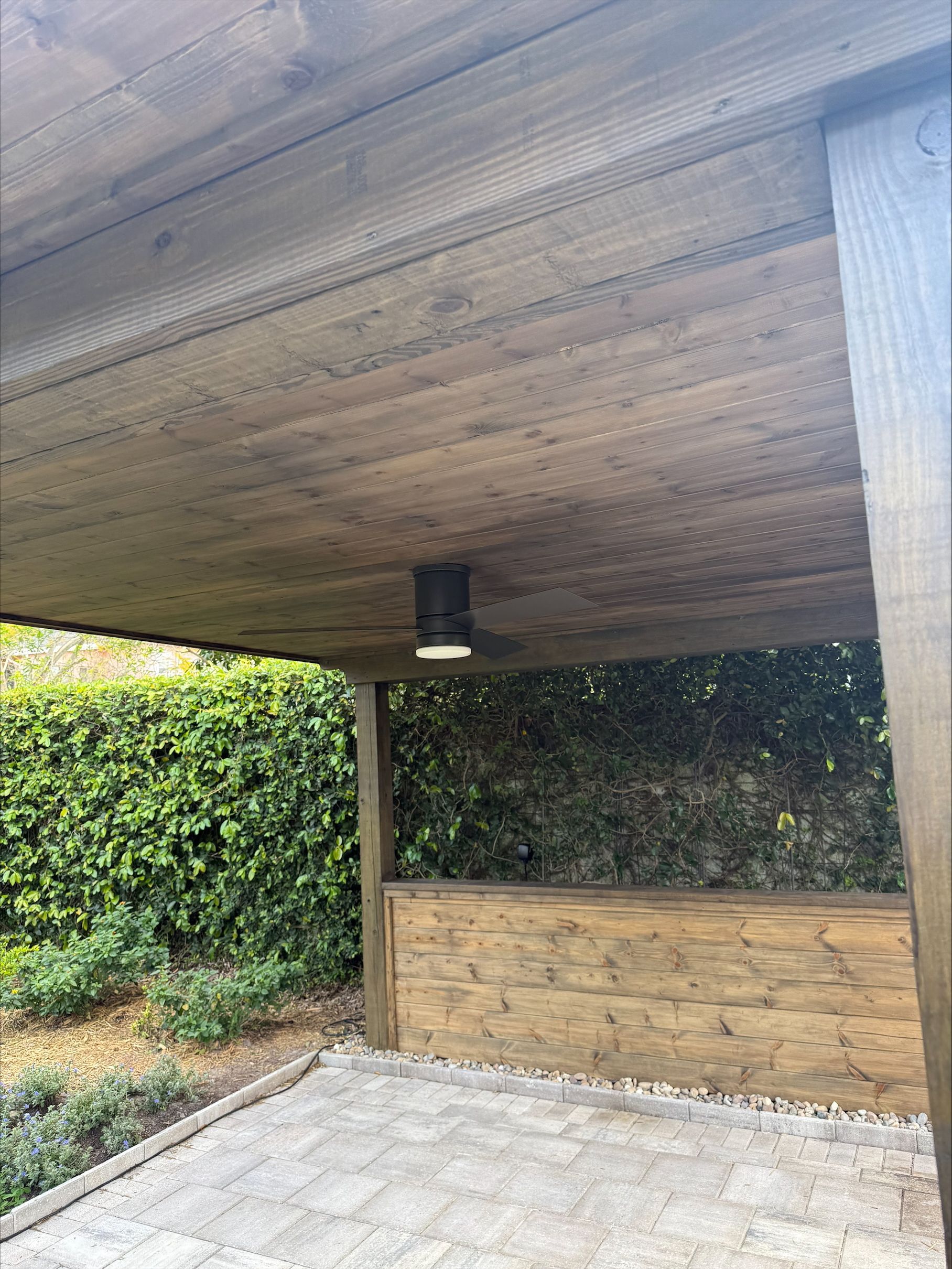 There is a ceiling fan hanging from the ceiling of a wooden structure.