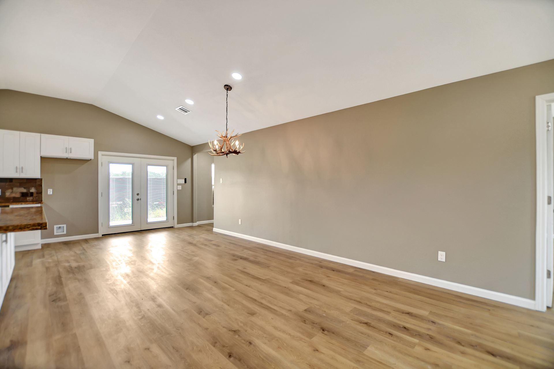 Empty living room with vaulted ceiling, hardwood floors, and French doors.