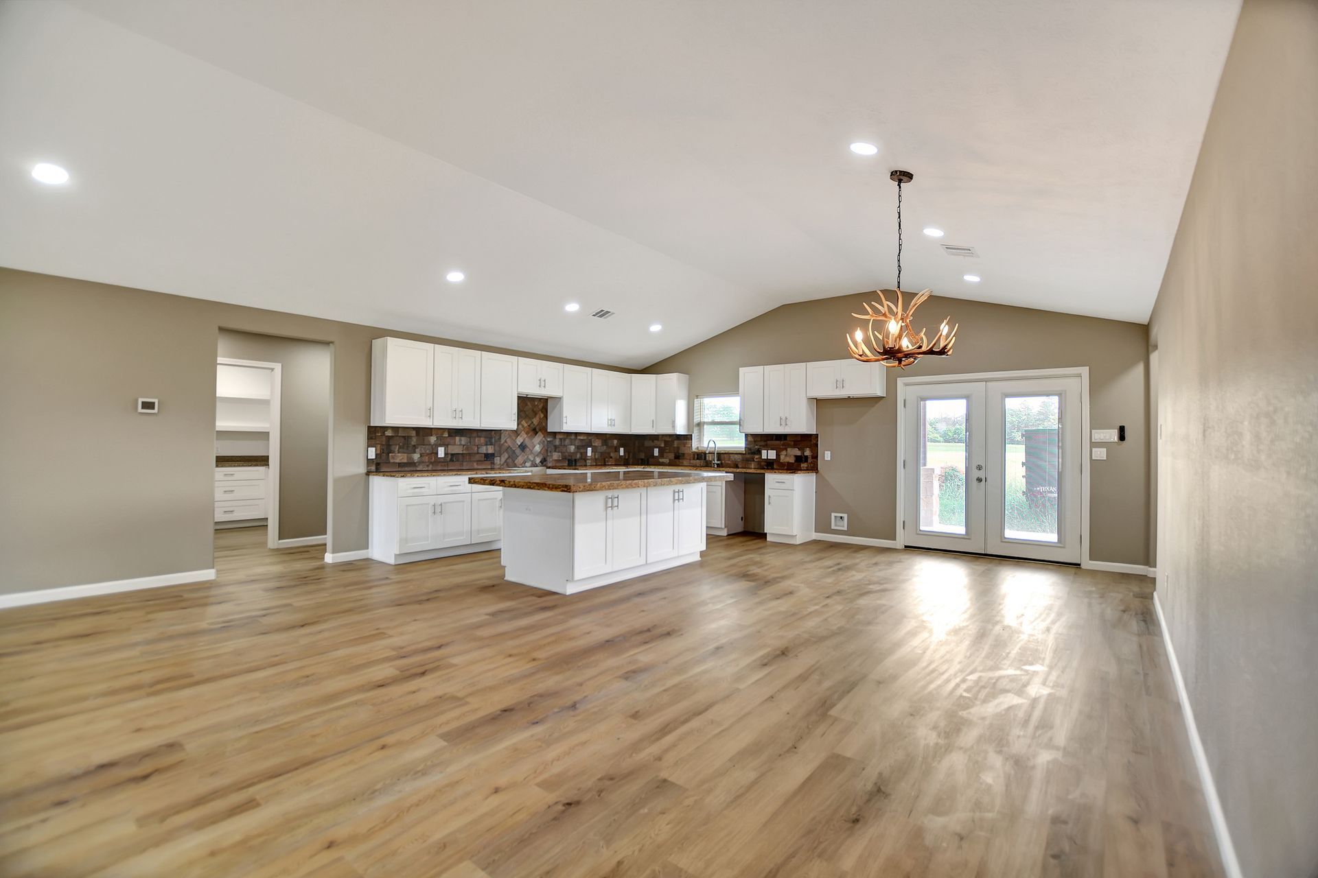 Spacious kitchen with white cabinets, wood floors, and a chandelier. French doors lead outside.