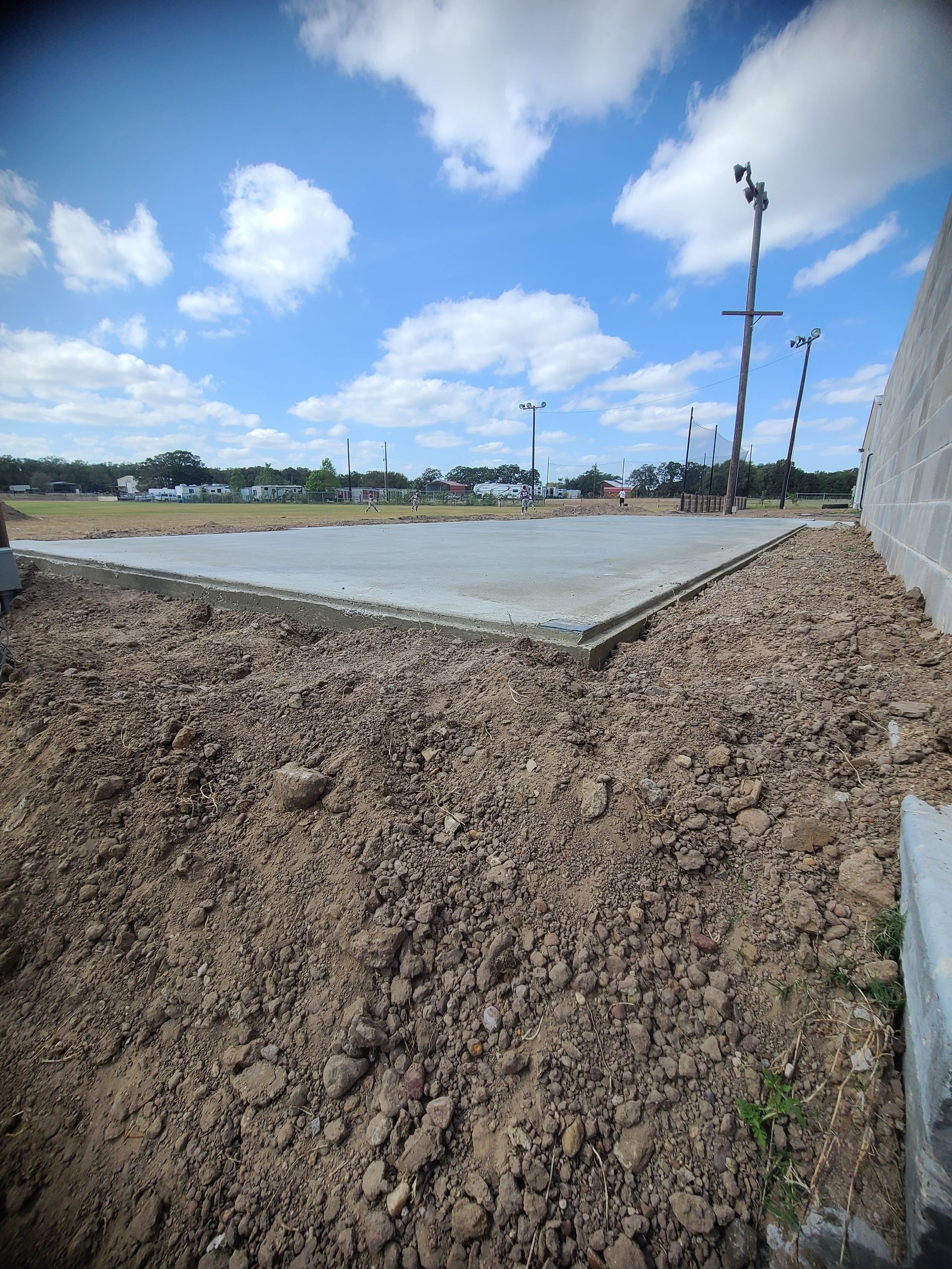 Construction site with concrete slab and dirt mound under a blue sky.