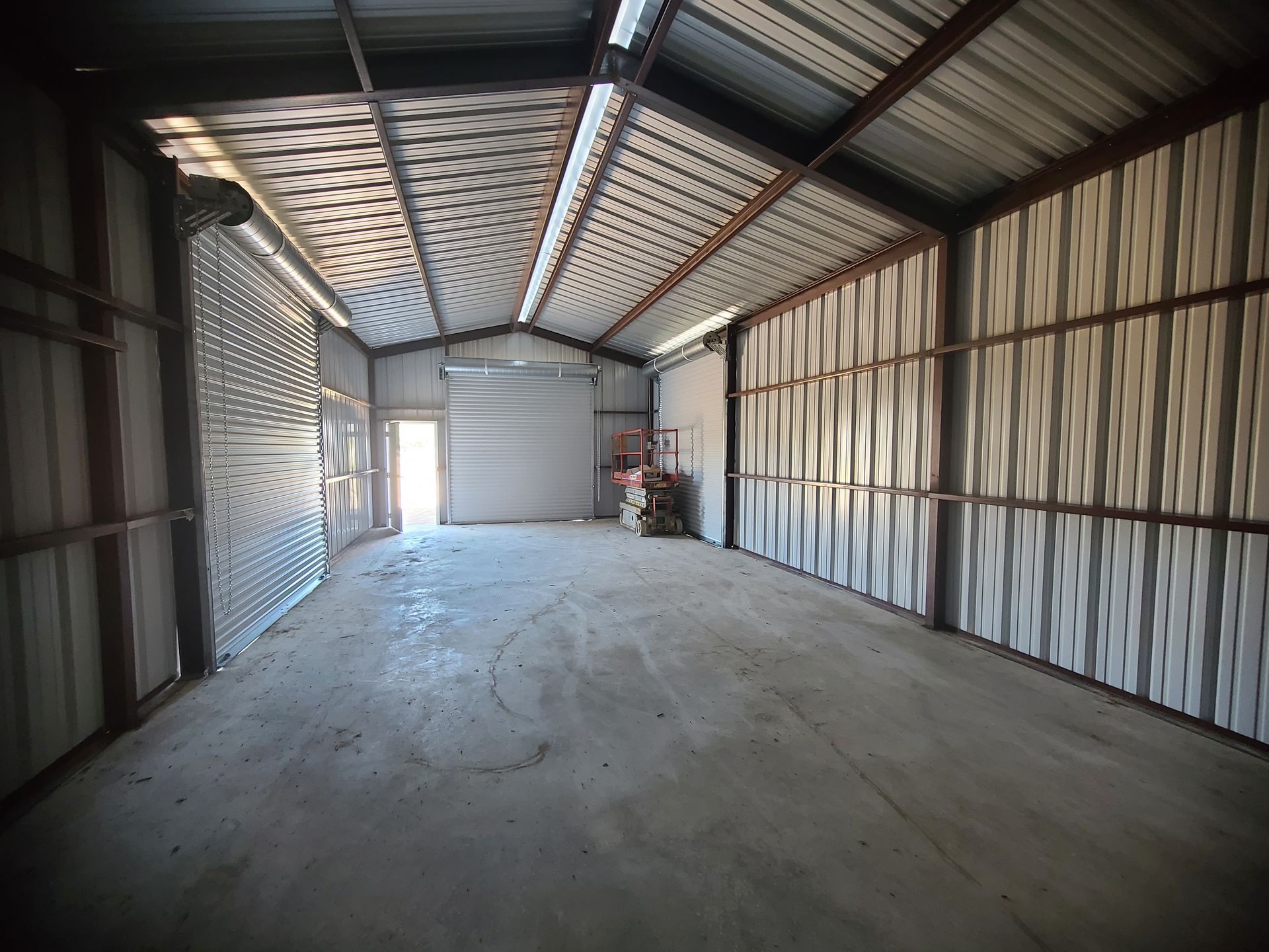 Interior of an empty metal warehouse with concrete floor, open garage door at the far end.