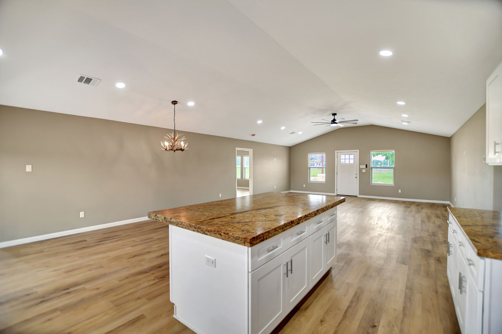 Spacious kitchen with white cabinets, a granite island, and light wood floors.