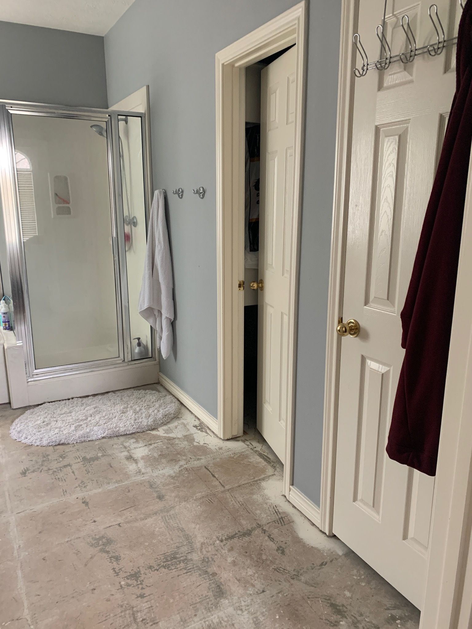 Bathroom with a shower, doorway, and a partially finished floor. Blue walls and a dark red robe hang on the door.