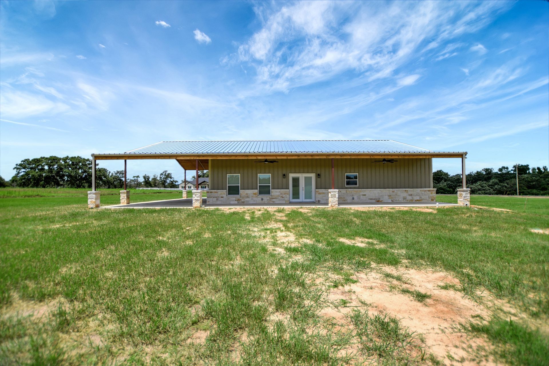 Single-story building with a long porch in a grassy field under a cloudy sky.