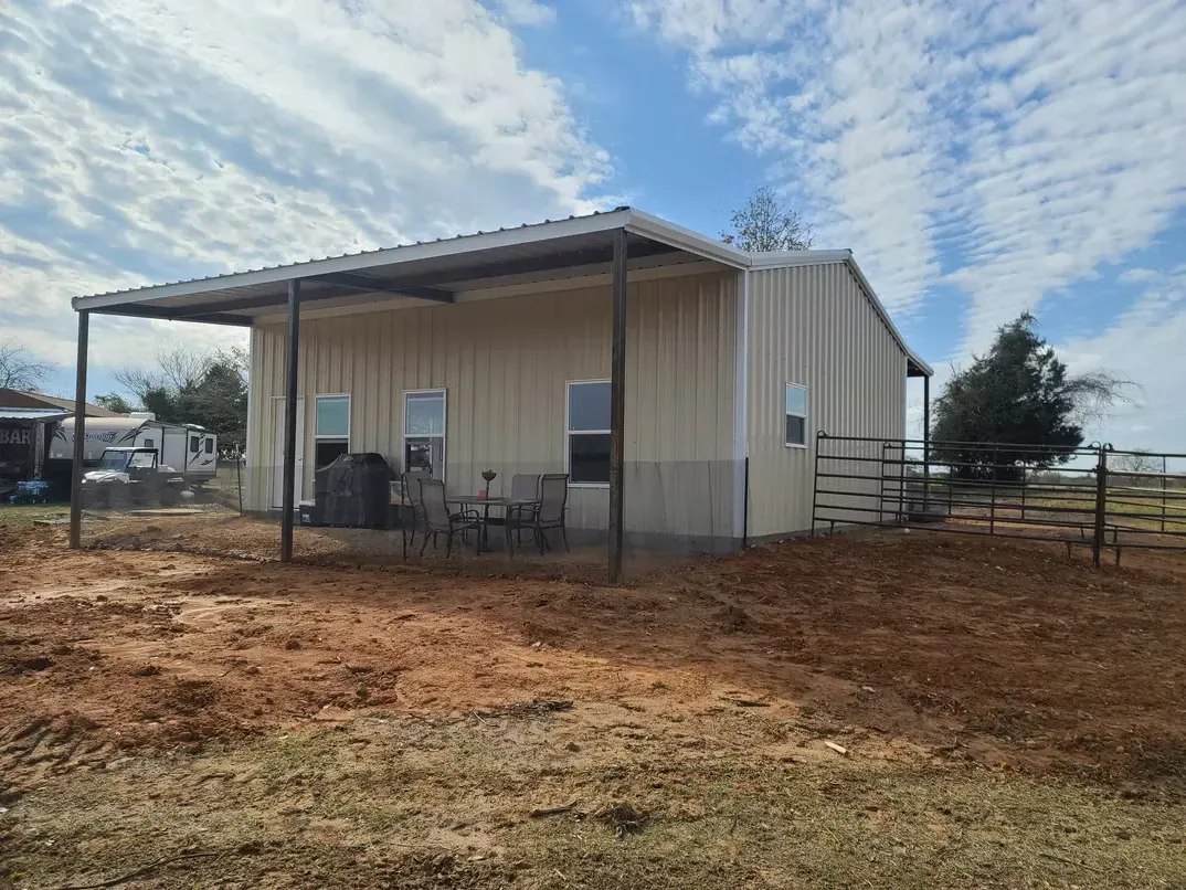 A small house with a porch is sitting in the middle of a dirt field.