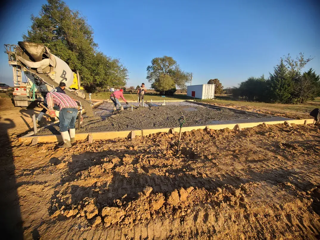 A concrete truck is pouring concrete into a dirt field.