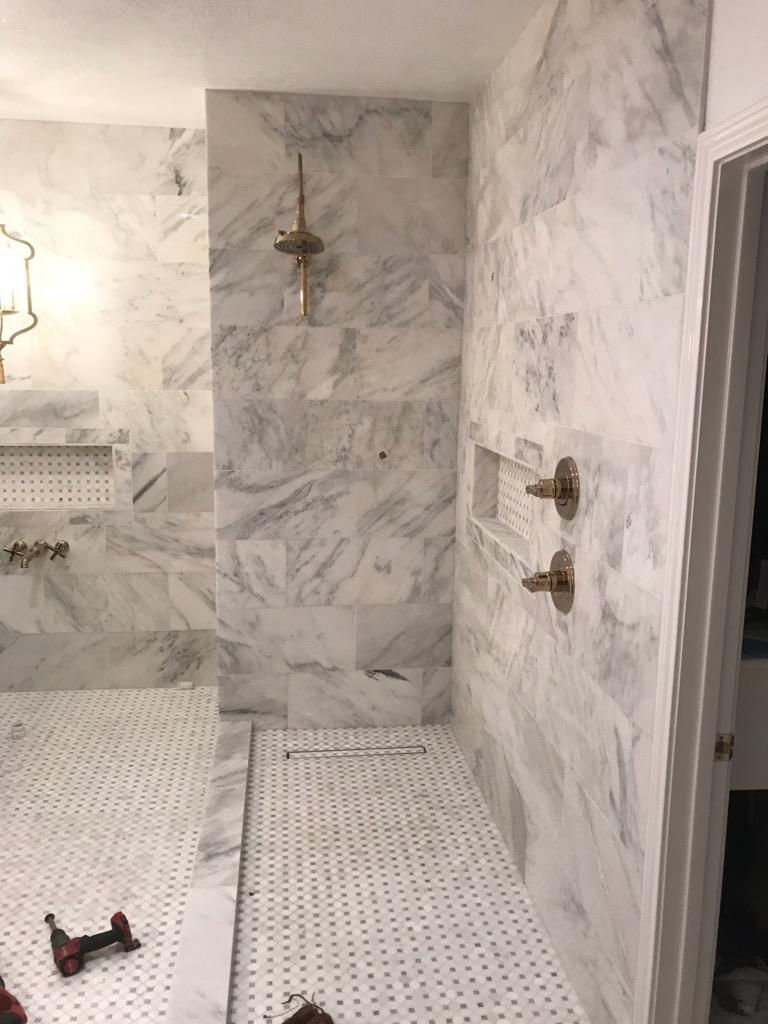 Marble-tiled shower with gold fixtures; includes a showerhead, controls, and a built-in shelf.