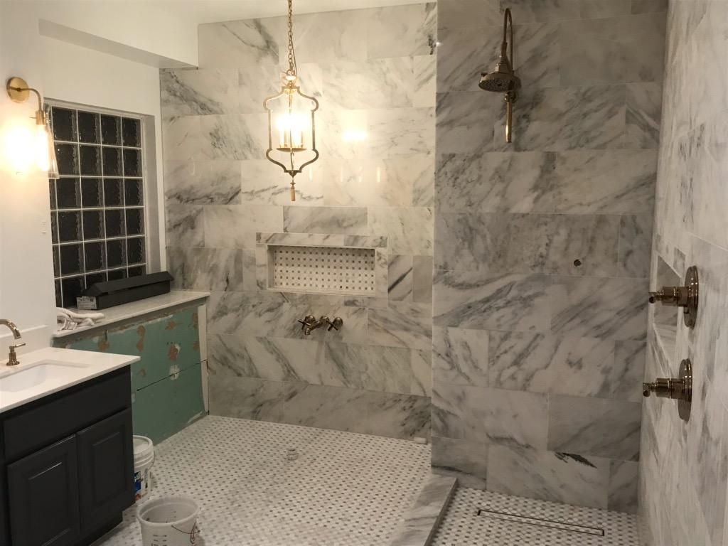 Bathroom with marble tile walls, shower fixture, vanity, and window. Gold light fixture hangs from ceiling.