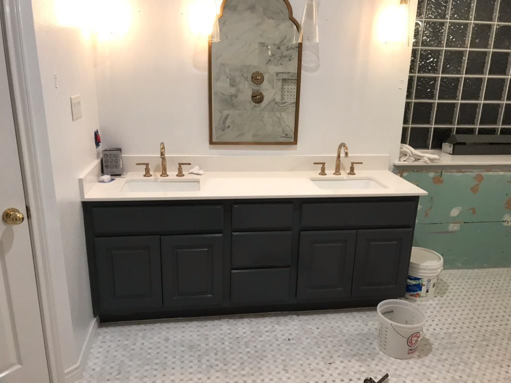 Bathroom with a dark blue vanity, white countertop, two sinks, and gold faucets, beneath a large mirror.