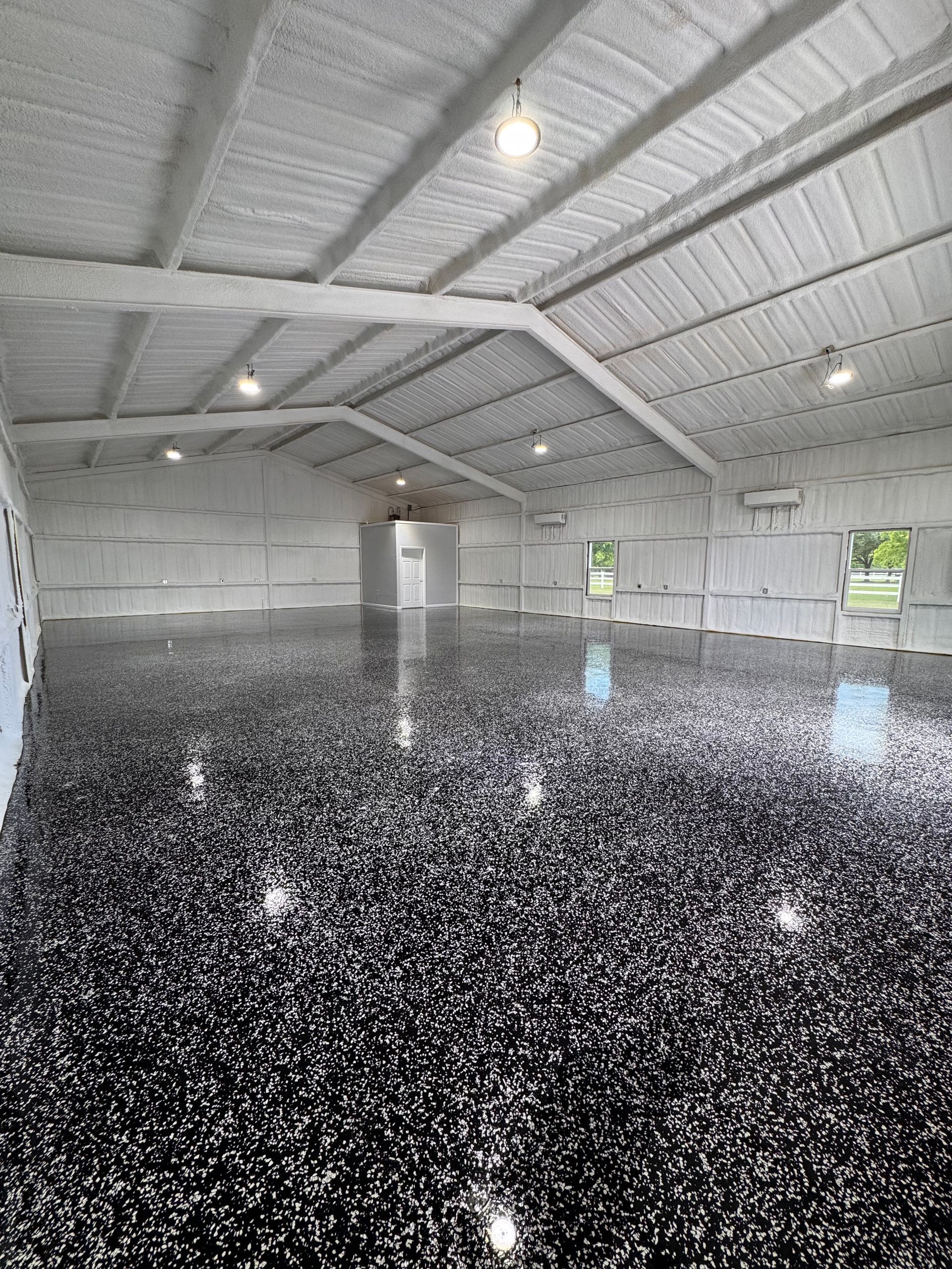 Interior of a large building, featuring a glossy, speckled black floor and white insulated walls and ceiling.