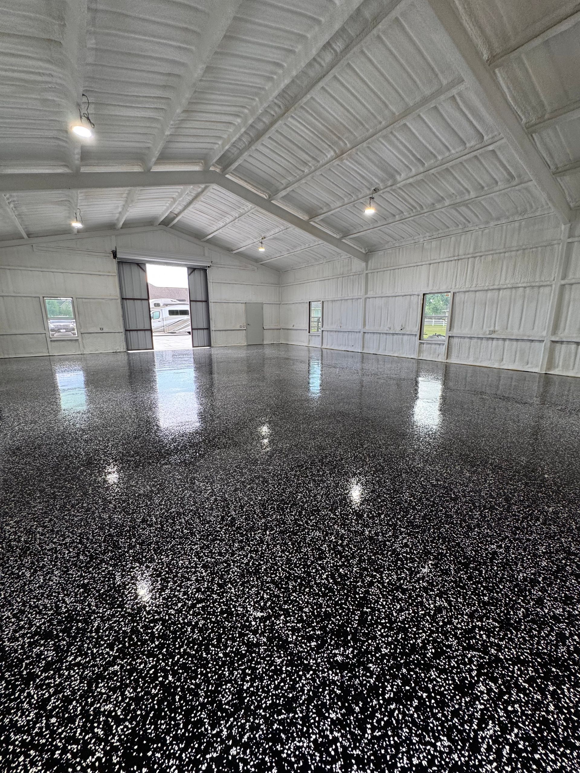 Interior of a large warehouse with a shiny black and white speckled epoxy floor and insulated white walls and ceiling.