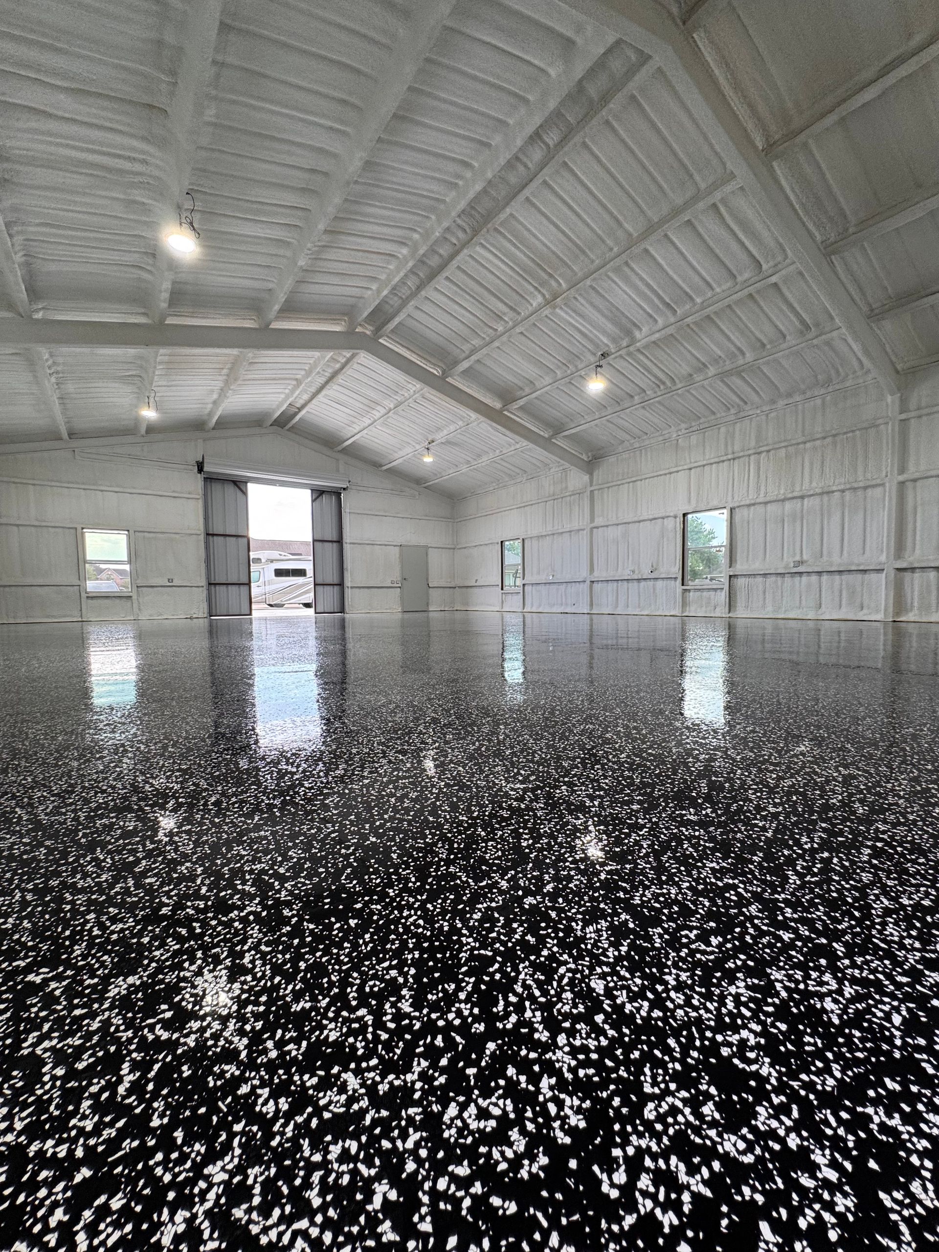 Brightly lit industrial building with speckled black and white floor and white foam insulation on walls and ceiling.