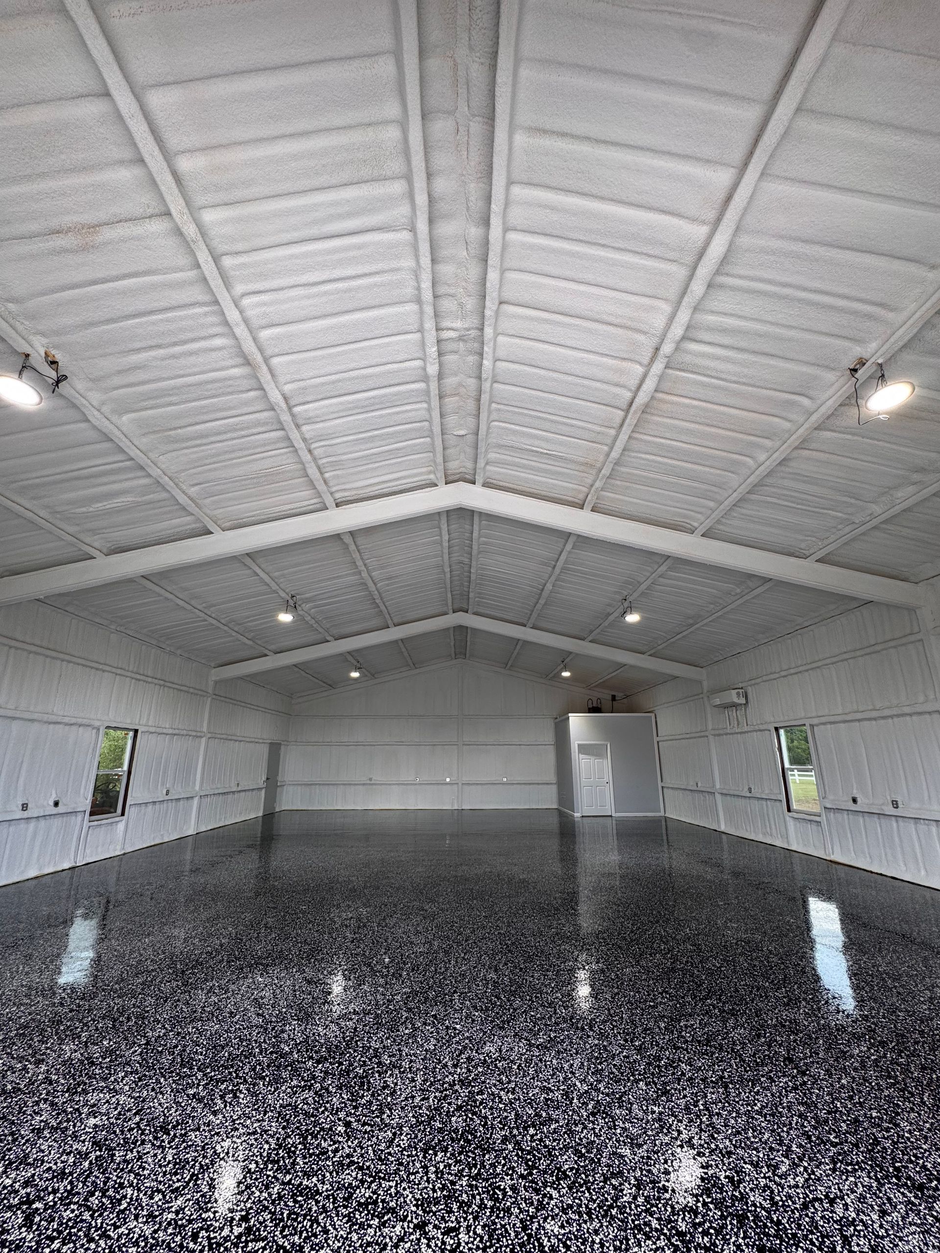 Interior of a large, white garage with a shiny, dark speckled floor and recessed lighting.
