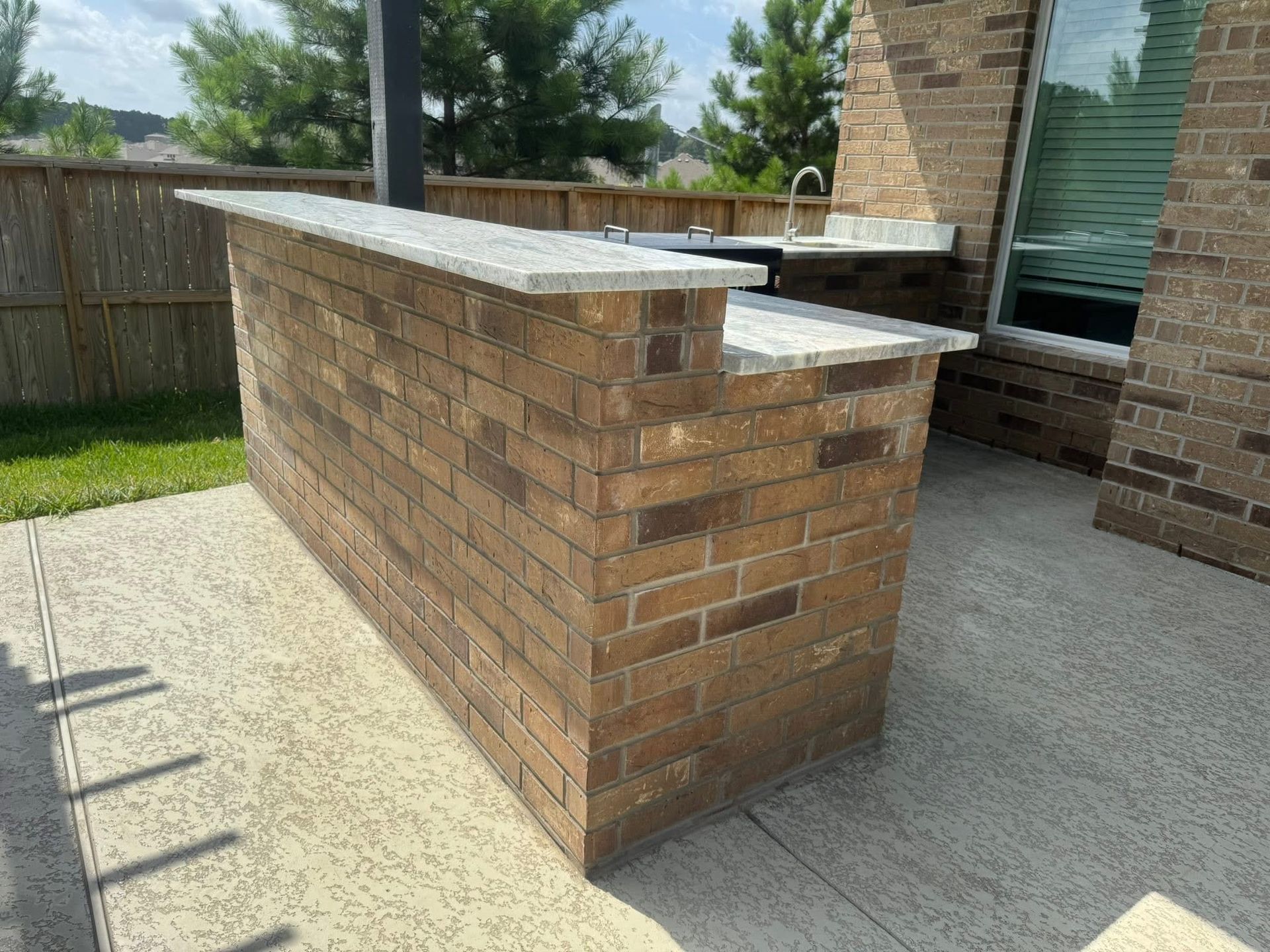 Brick outdoor bar with a gray countertop next to a brick wall.