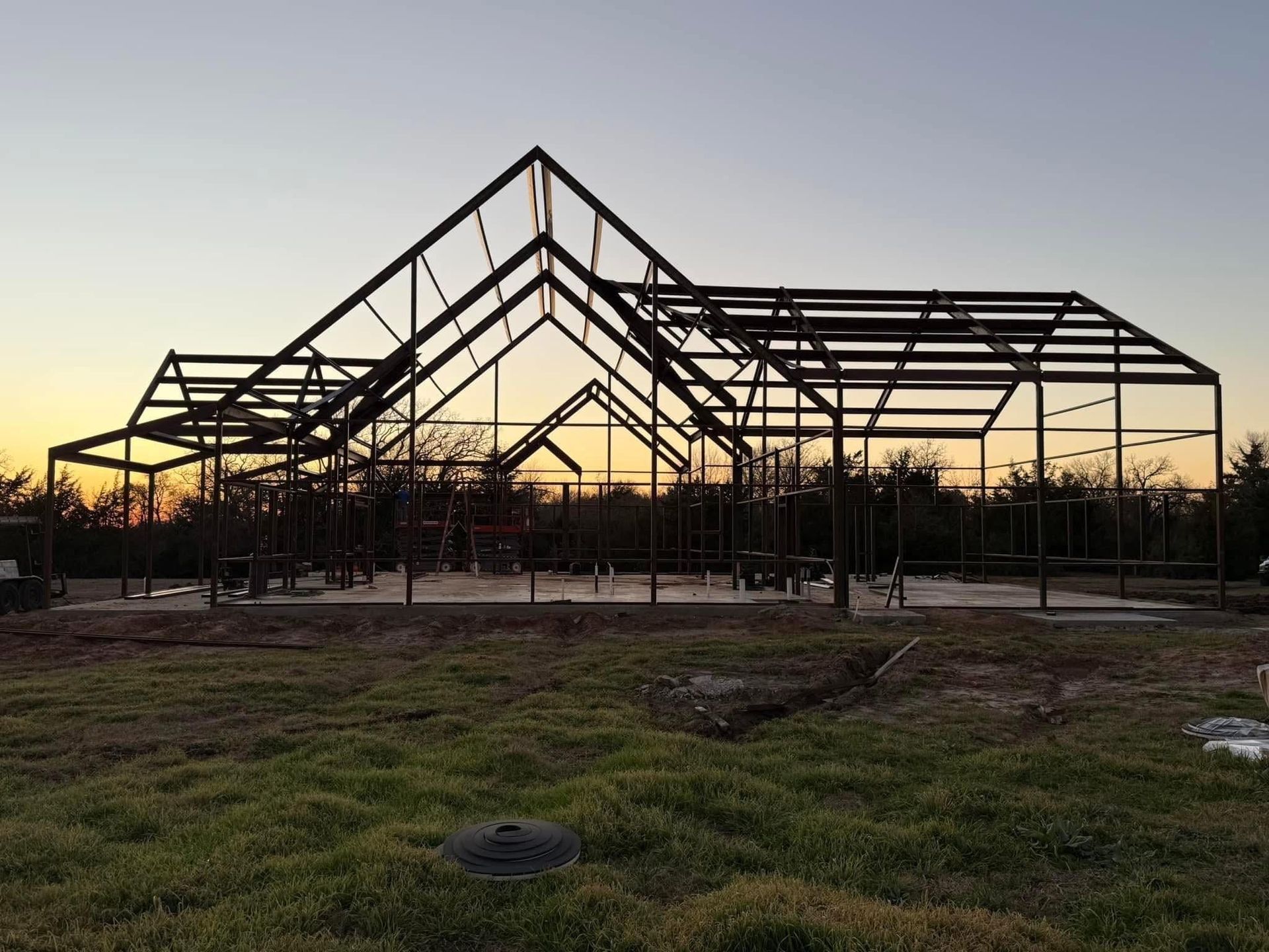 Steel frame of a house under construction against a sunset sky.