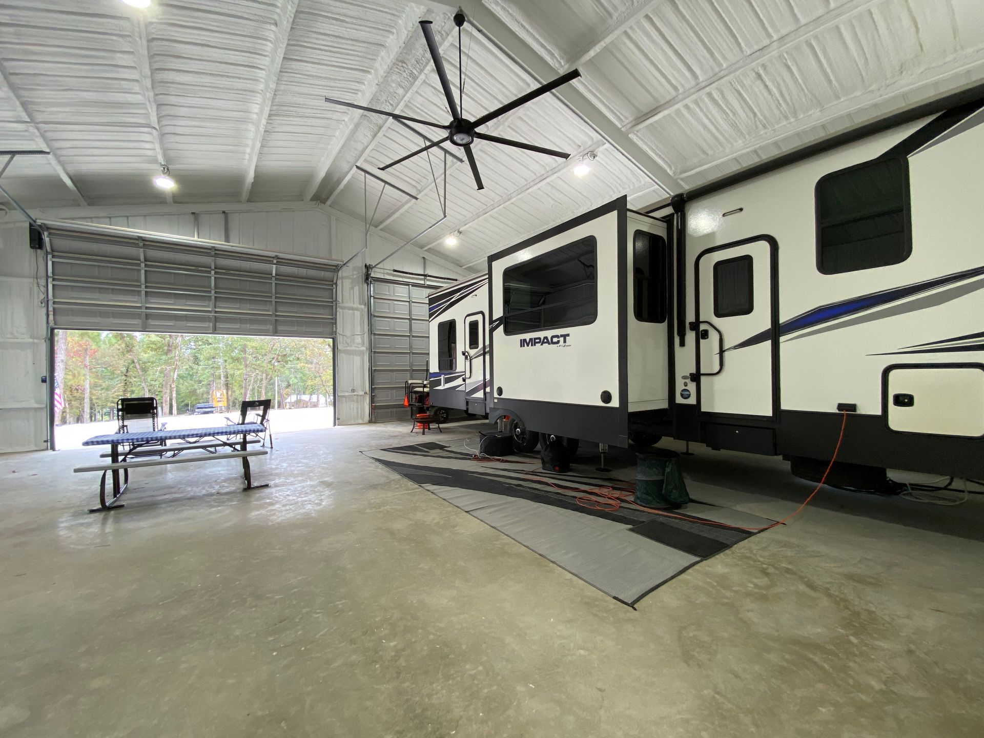 Two RVs parked inside a large, white metal building with a picnic table.