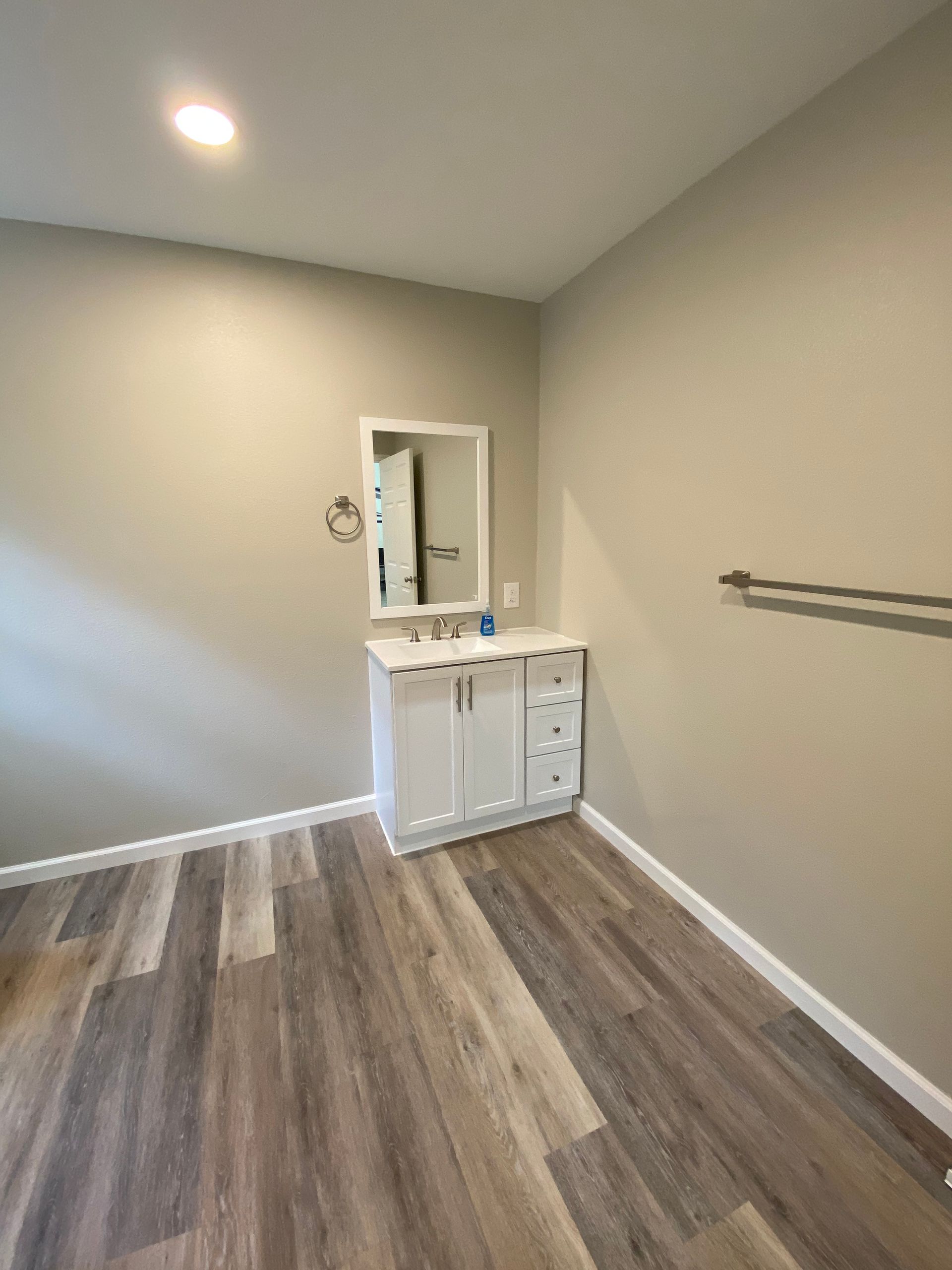White vanity with mirror in a bathroom, light walls, wood-look floor, silver towel bar.