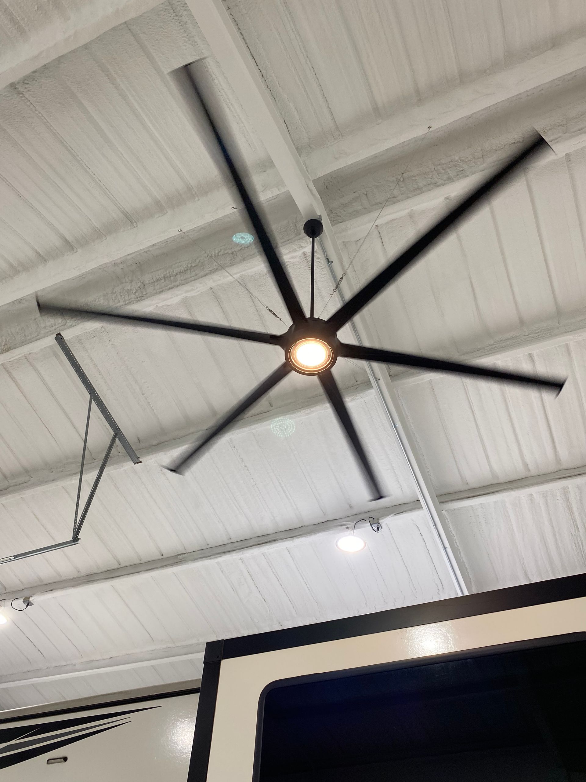 Large black ceiling fan with six blades spinning, centered on a white ceiling.