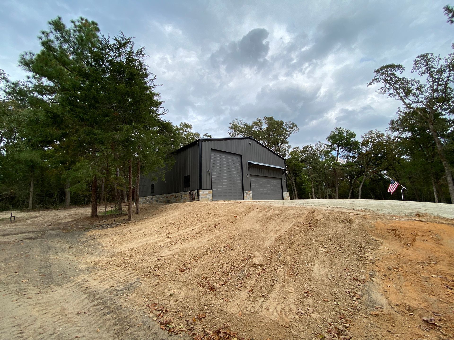 Dark gray metal building with two garage doors, set on a hill under a cloudy sky.