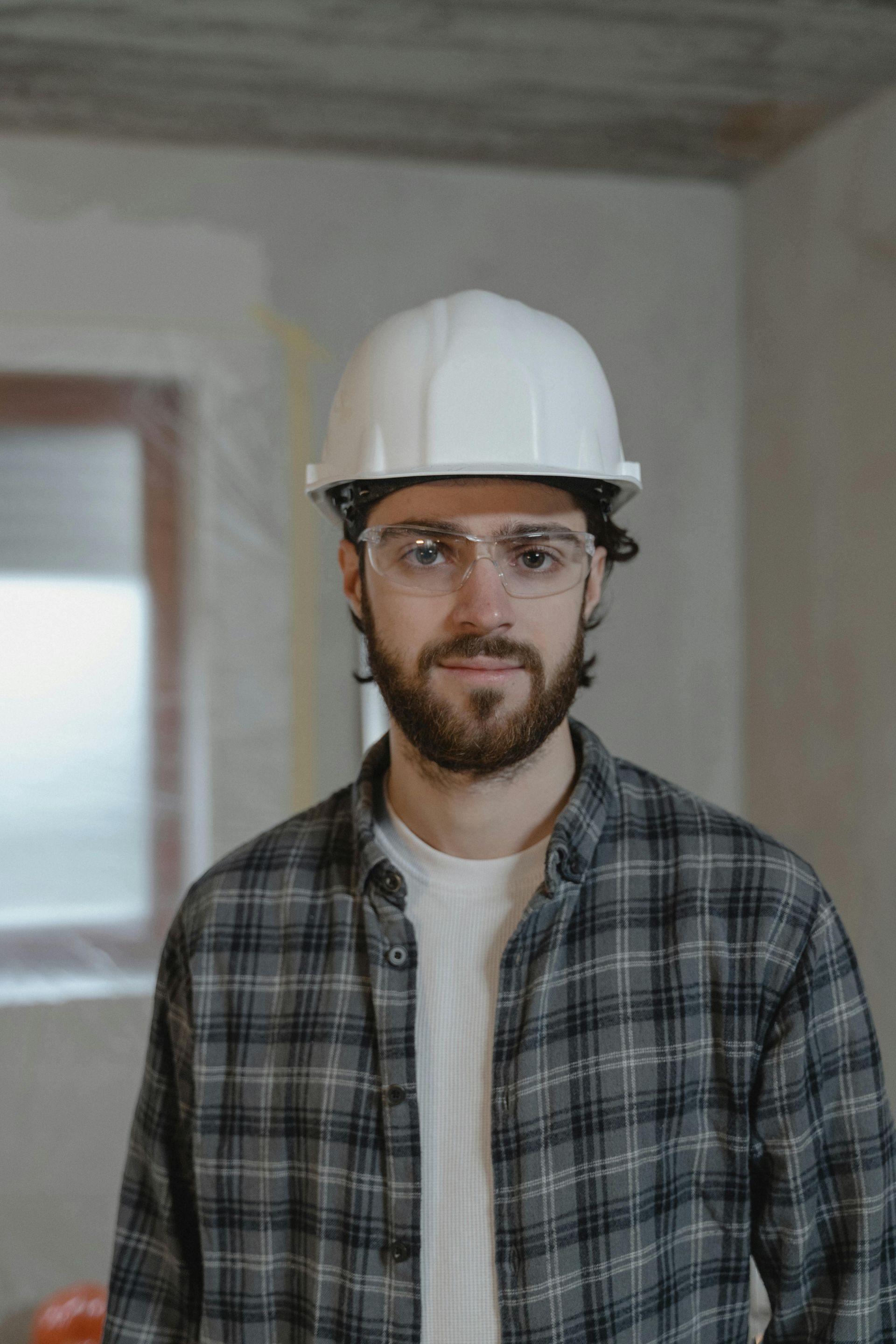 A man wearing a hard hat and glasses is standing in a room.