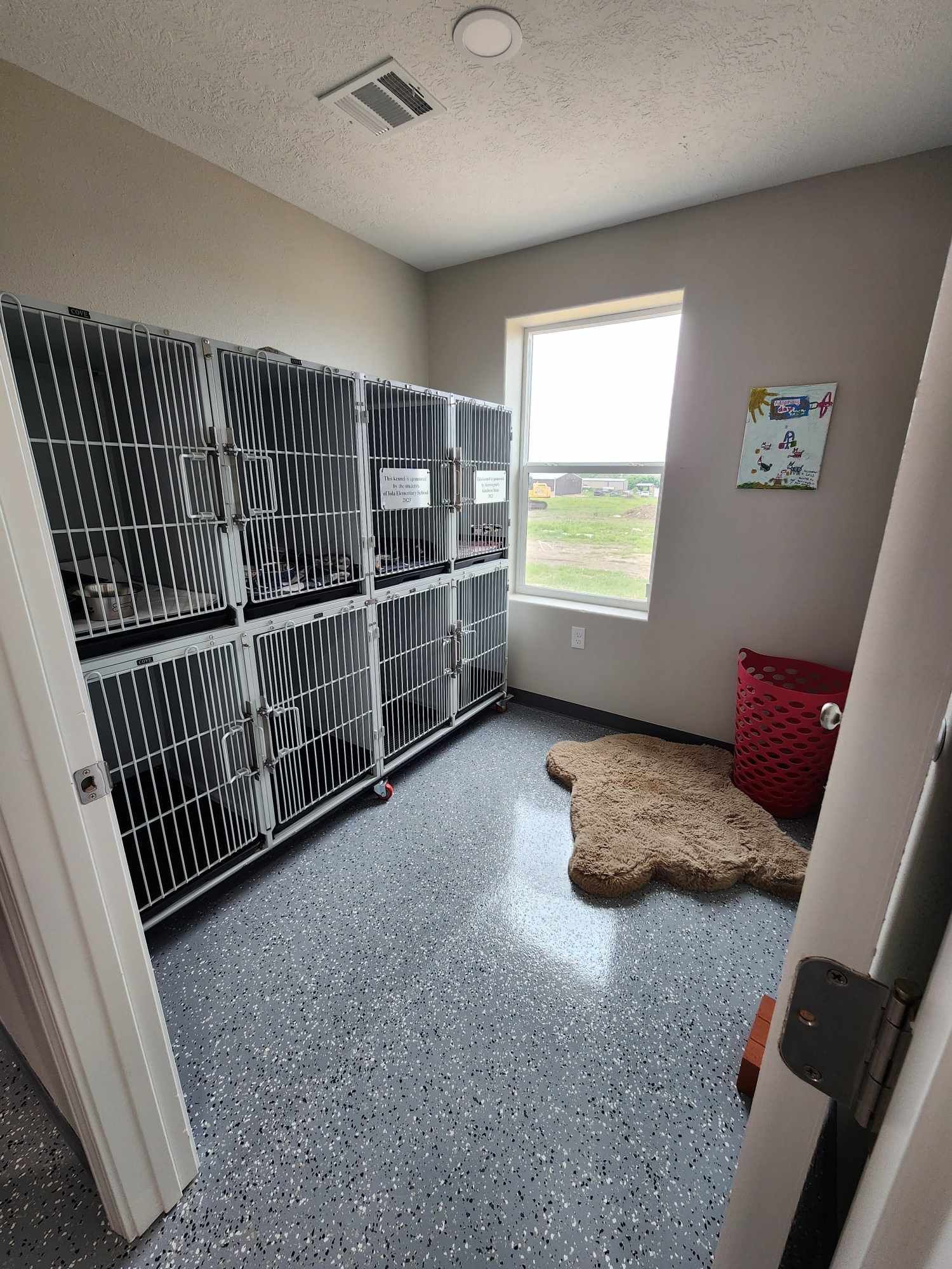 Dog kennel room with metal cages, speckled floor, a window, and a dog bed.