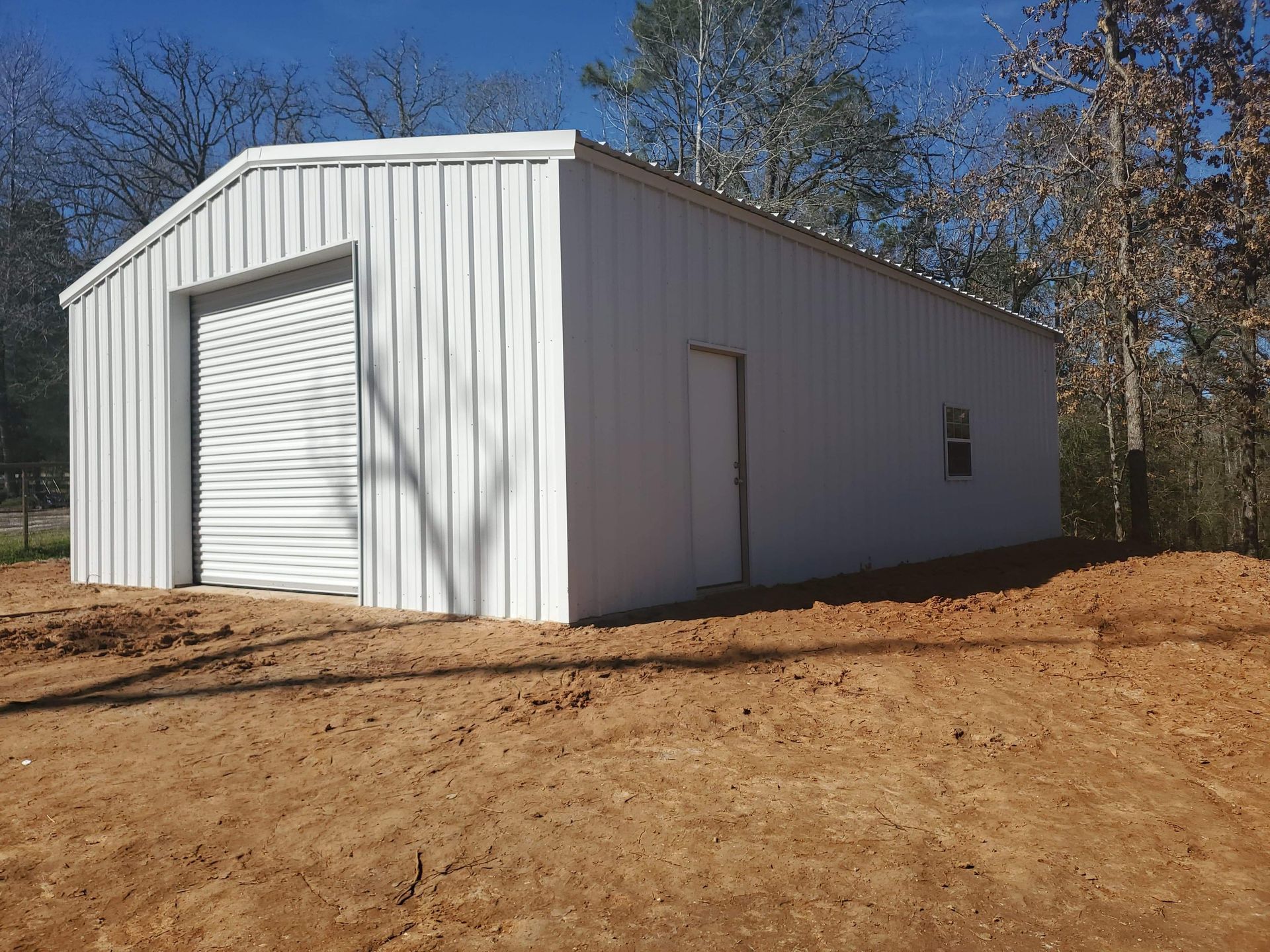 White metal building with a garage door and small window. Located in a clearing with trees.