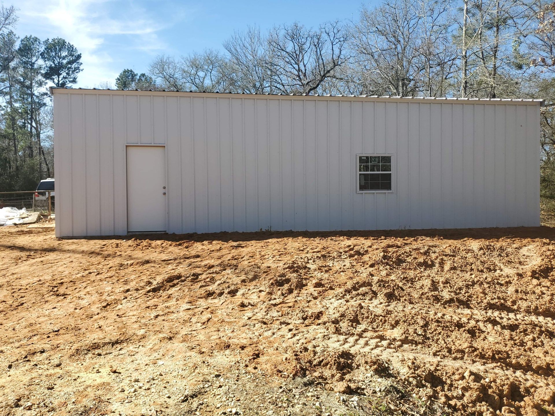 White metal storage building with a door and small window in a dirt lot.