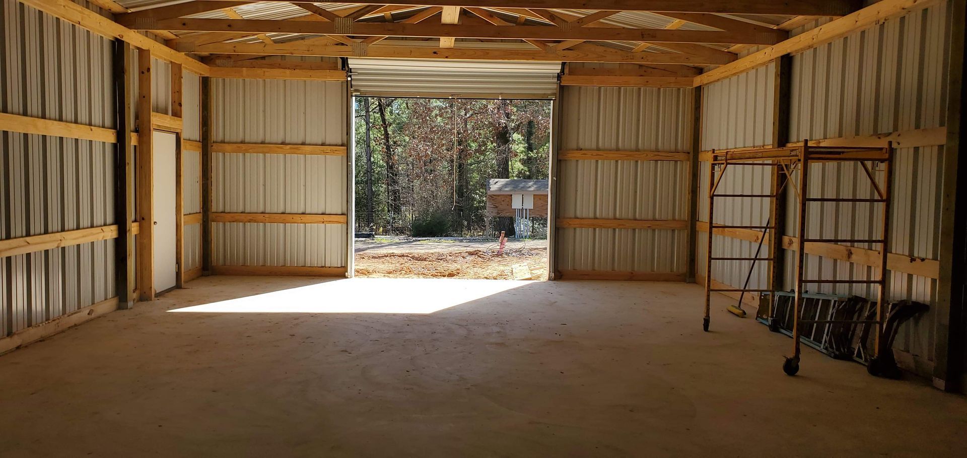 Inside of a metal shed with an open doorway, showing a concrete floor and exposed wooden beams.