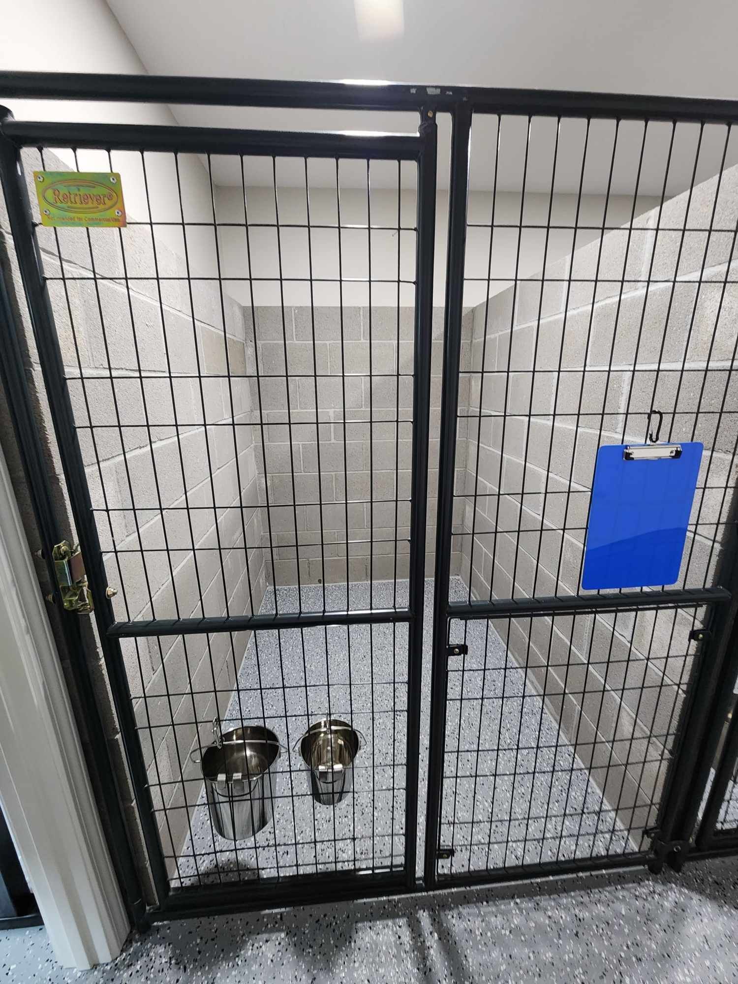 Dog kennel with metal gates and food bowls. Interior with tiled walls and blue clipboard.