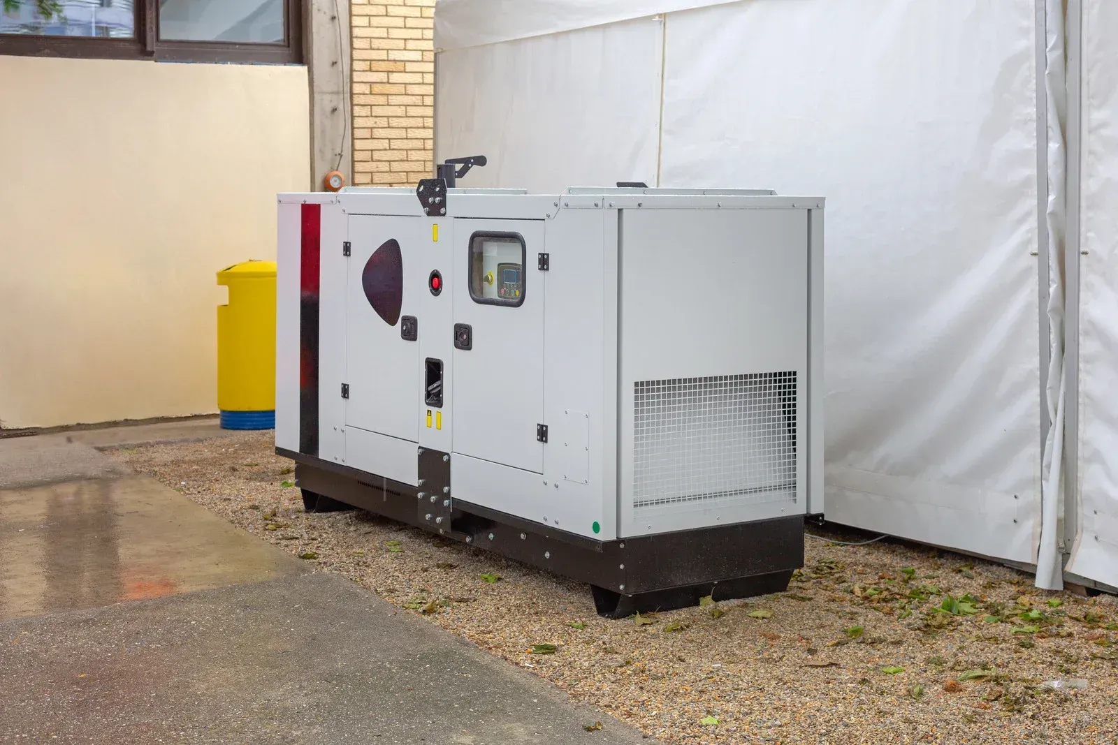 A generator is sitting outside of a building next to a tent.