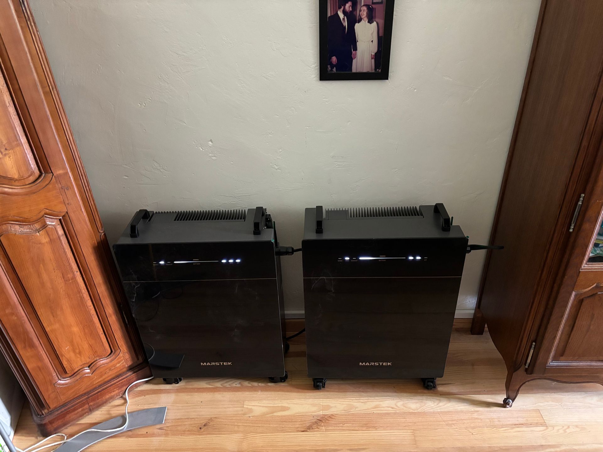 Deux électroménagers rectangulaires noirs sur roulettes près d'un meuble en bois. Photo encadrée ci-dessus.